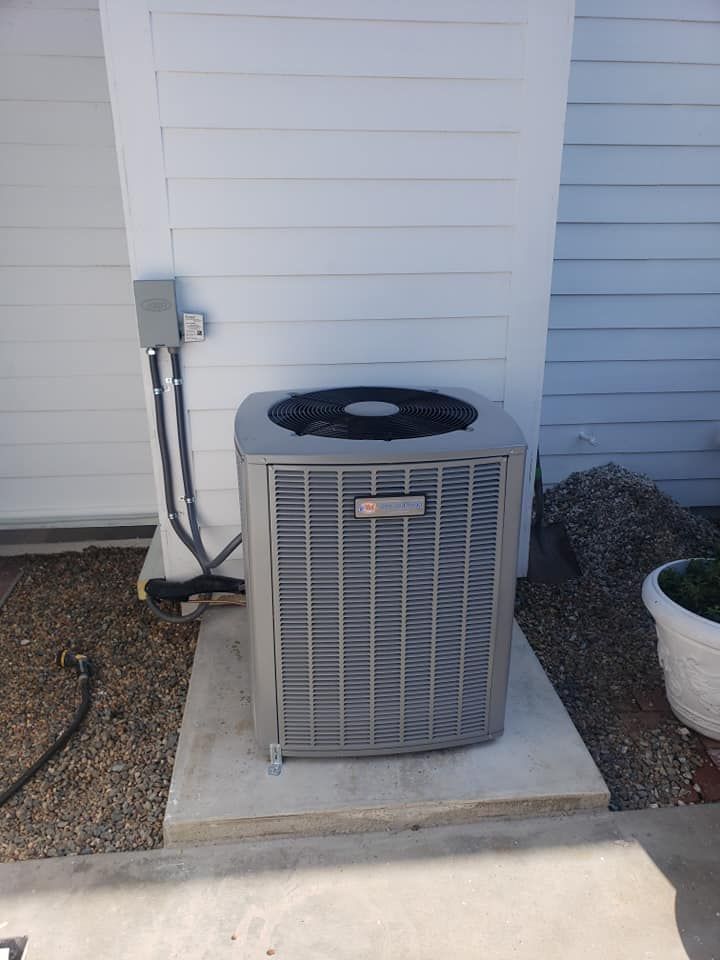 A gray air conditioner is sitting outside of a white house.