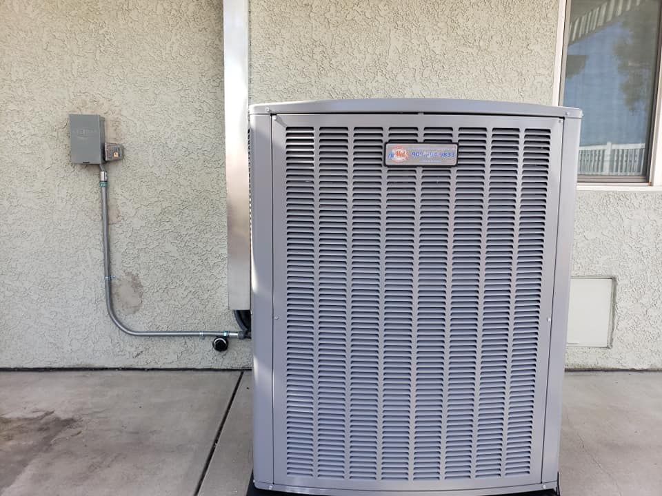 A gray air conditioner is sitting outside of a building