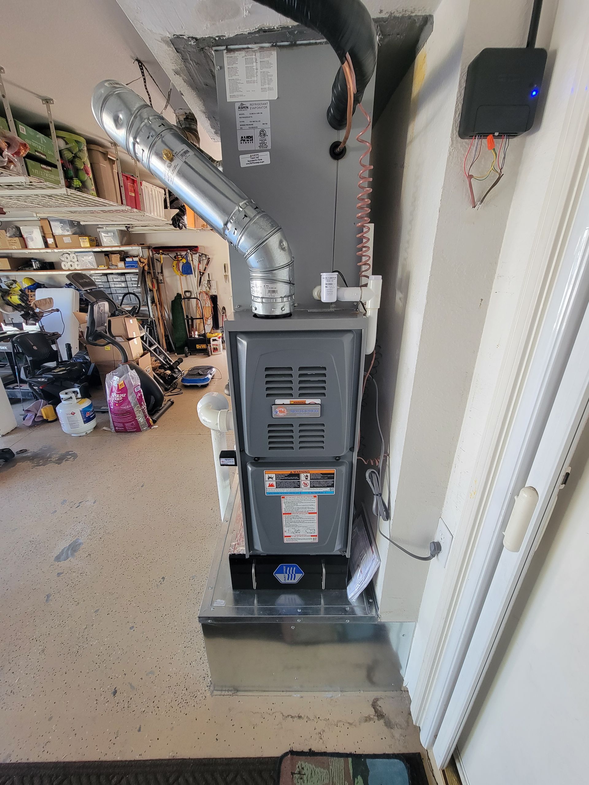 A furnace is sitting on the side of a wall in a garage.