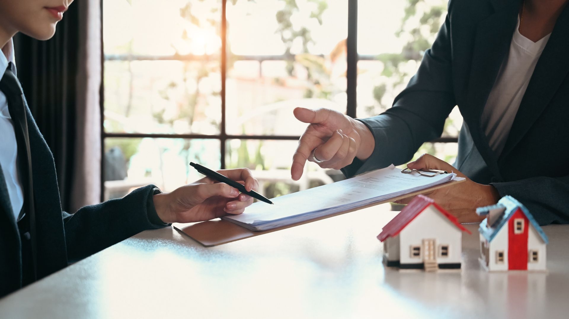 Two people reviewing a house contract at a desk with a small model home in the foreground
