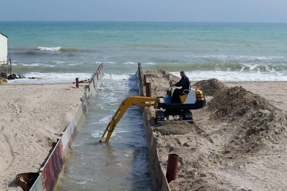 A Worker Operates a Mini Excavator Digging a Trench on a Beach Near the Ocean — Boland Contracting In Bourke, NSW