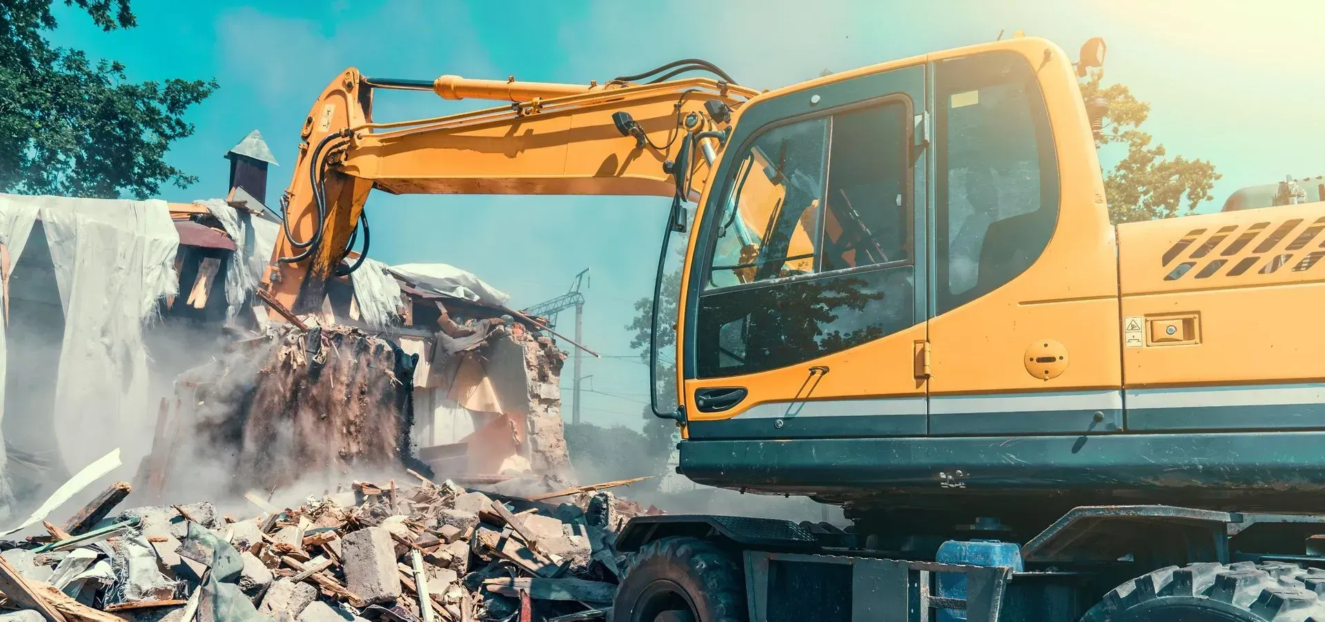 A Yellow Excavator Demolishes a Building Generating Dust and Rubble — Boland Contracting In Cobar, NSW