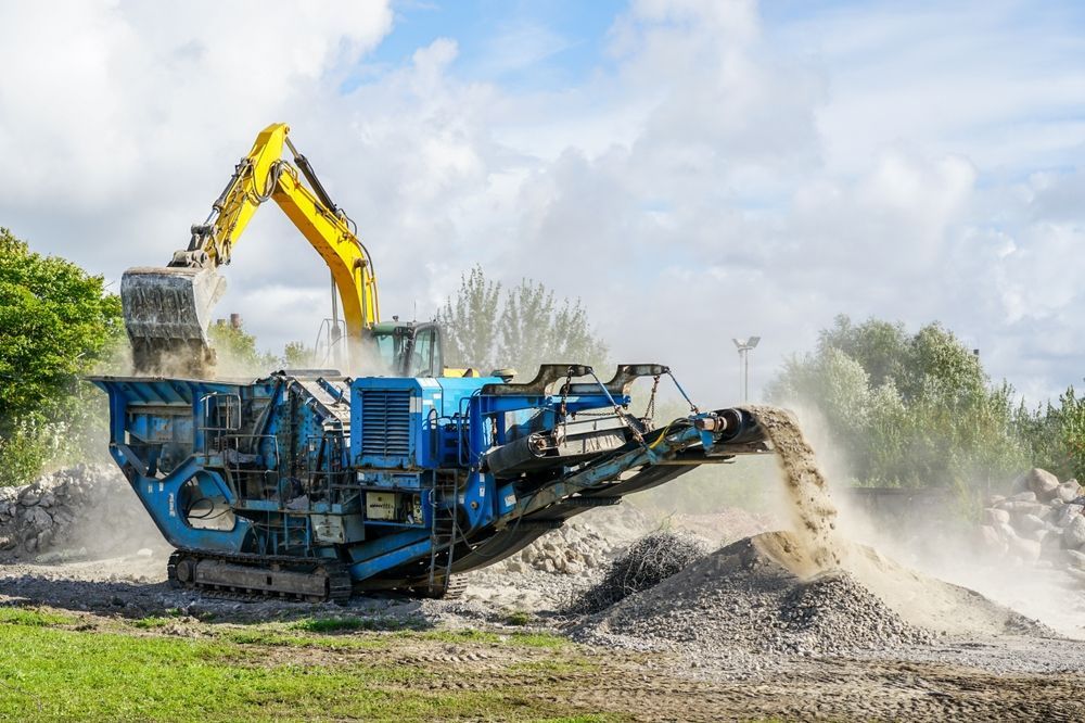 Excavator Dumping Rocks Into a Blue Mobile Crusher, Producing Gravel Outdoors — Boland Contracting In Wellington, NSW