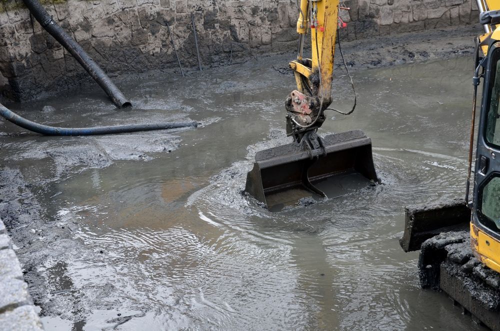 Excavator bucket scoops muddy water and sludge from a trench — Boland Contracting In Wellington, NSW