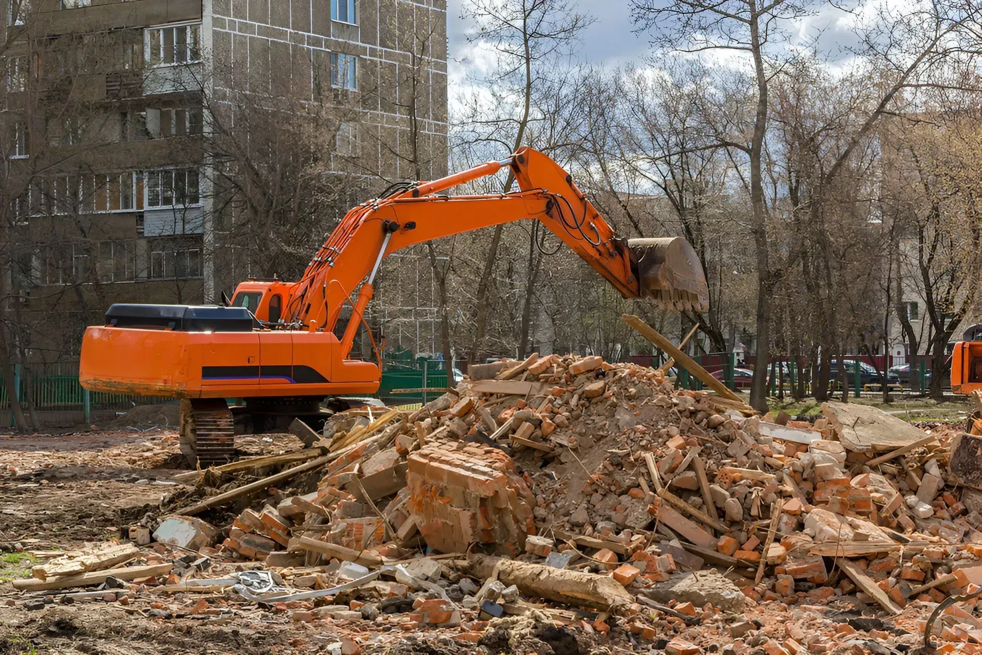Orange Excavator Demolishing Rubble Near a Multistory Building — Boland Contracting In Mudgee, NSW