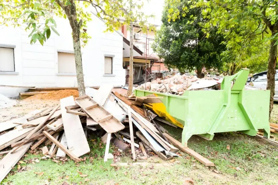 A Green Dumpster Filled With Debris Next to a House Under Construction — Boland Contracting In Bourke, NSW