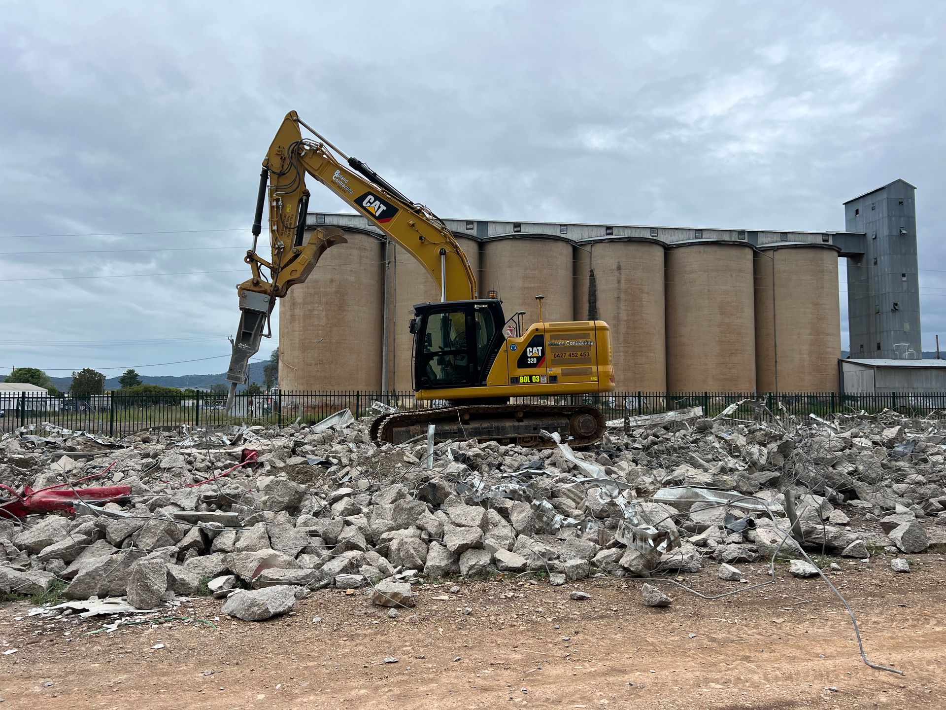 Yellow Excavator Dismantling a Building, Debris Scattered — Boland Contracting In Wellington, NSW