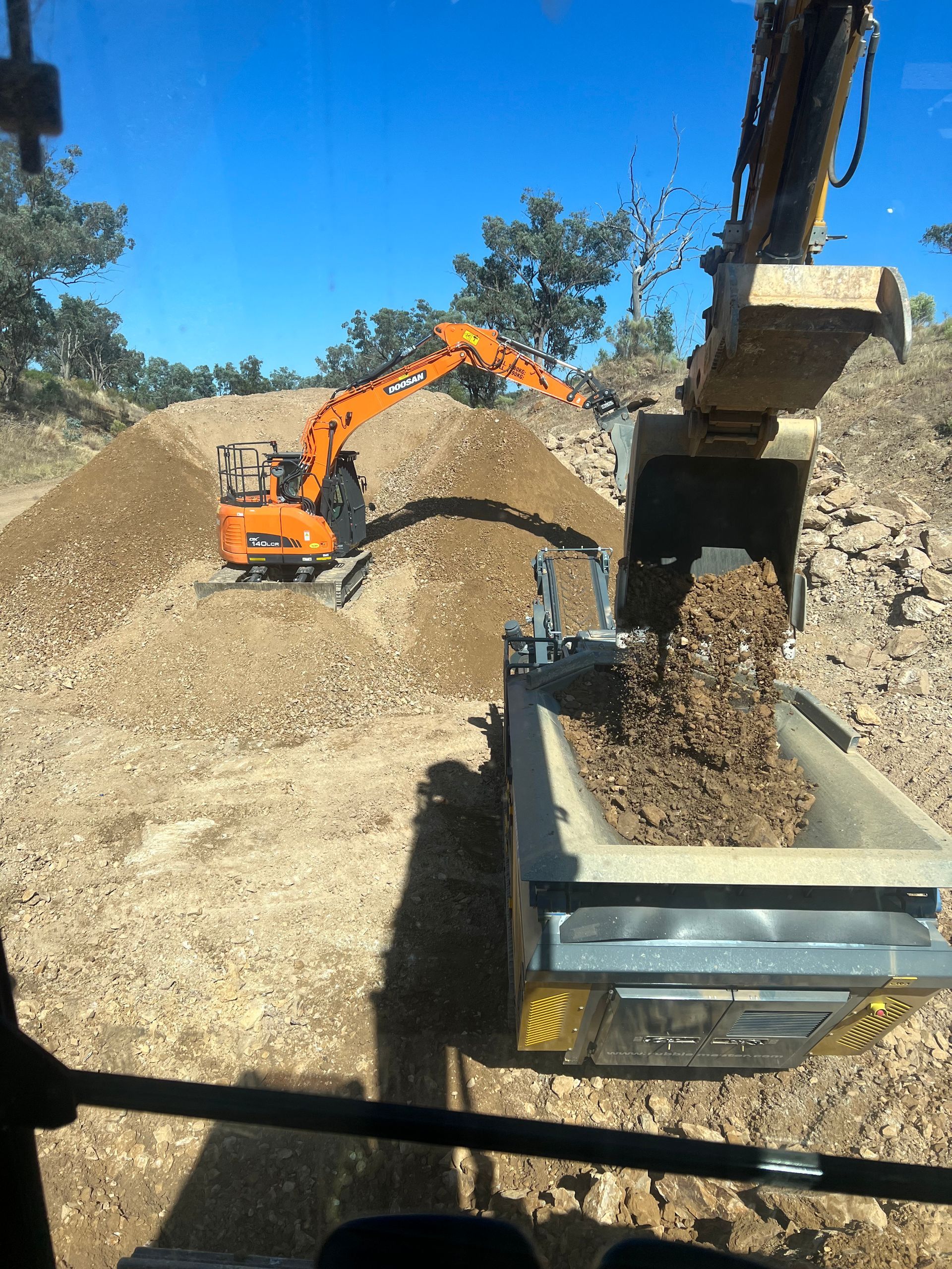 Orange Excavator Loading Dirt Into a Dump Truck at a Construction Site — Boland Contracting In Wellington, NSW