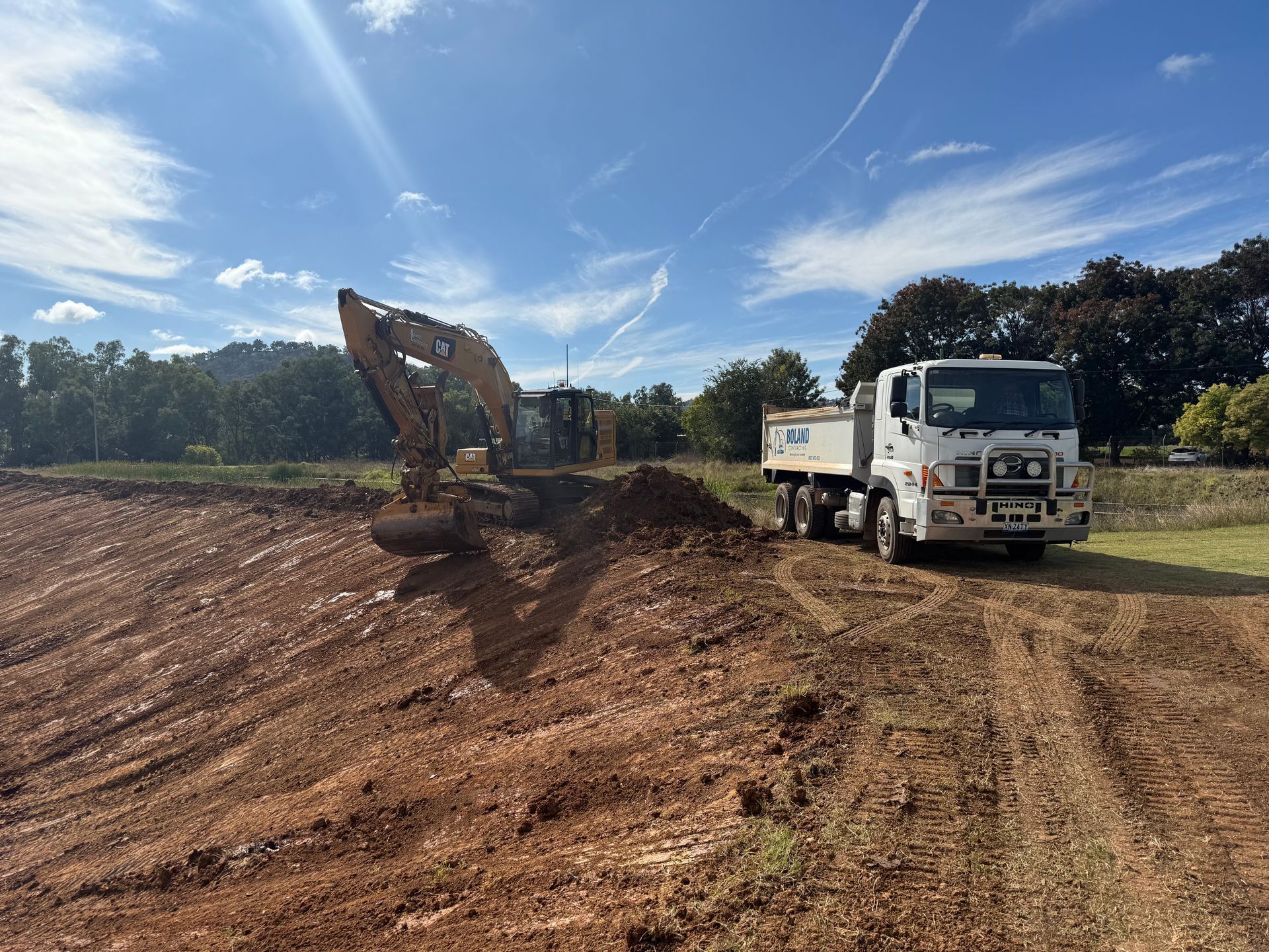 An Excavator Loading Dirt Into a White Dump Truck on a Construction Site — Boland Contracting In Wellington, NSW