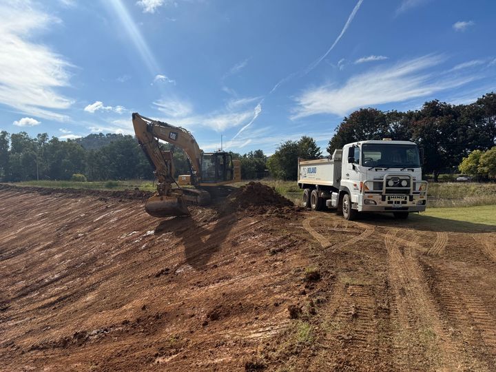 An Excavator Loading Dirt Into a White Dump Truck on a Construction Site — Boland Contracting In Wellington, NSW
