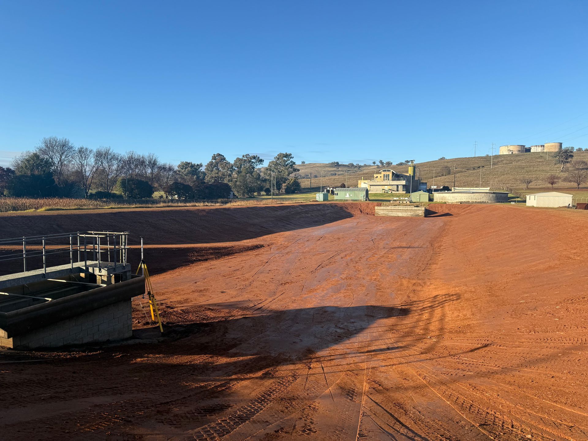A Dry Reddish-Brown Sediment Pond With Industrial Structures — Boland Contracting In Wellington, NSW