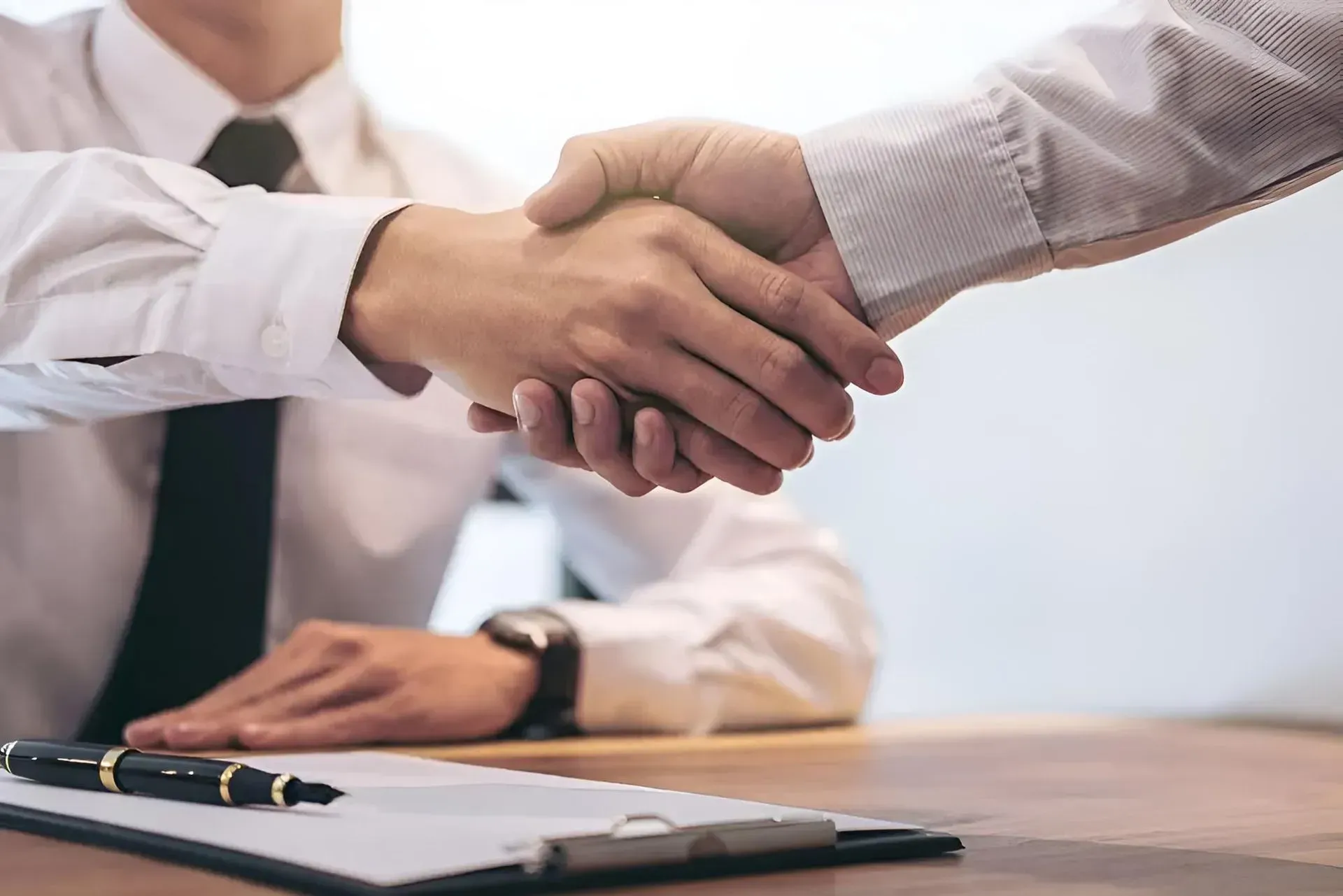 Two Men Shaking Hands Over a Desk With a Pen and Paperwork — Boland Contracting In Wellington, NSW