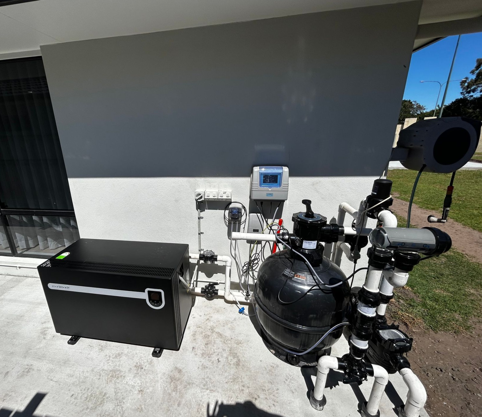 Outdoor Utility Equipment Beside a House: Black Tank, Control Panel, and Pipes on a Concrete Patio — Bromage Pool Heating in Palmview, QLD