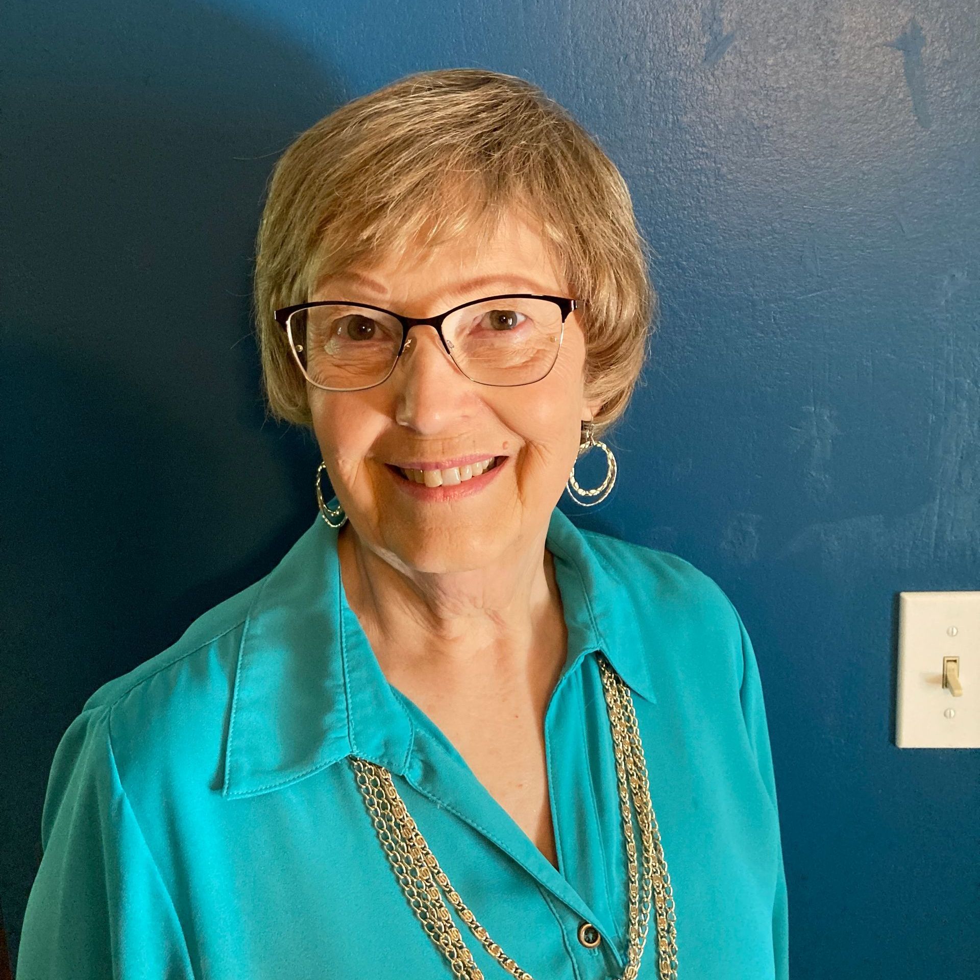 a woman wearing glasses and a blue shirt smiles for the camera