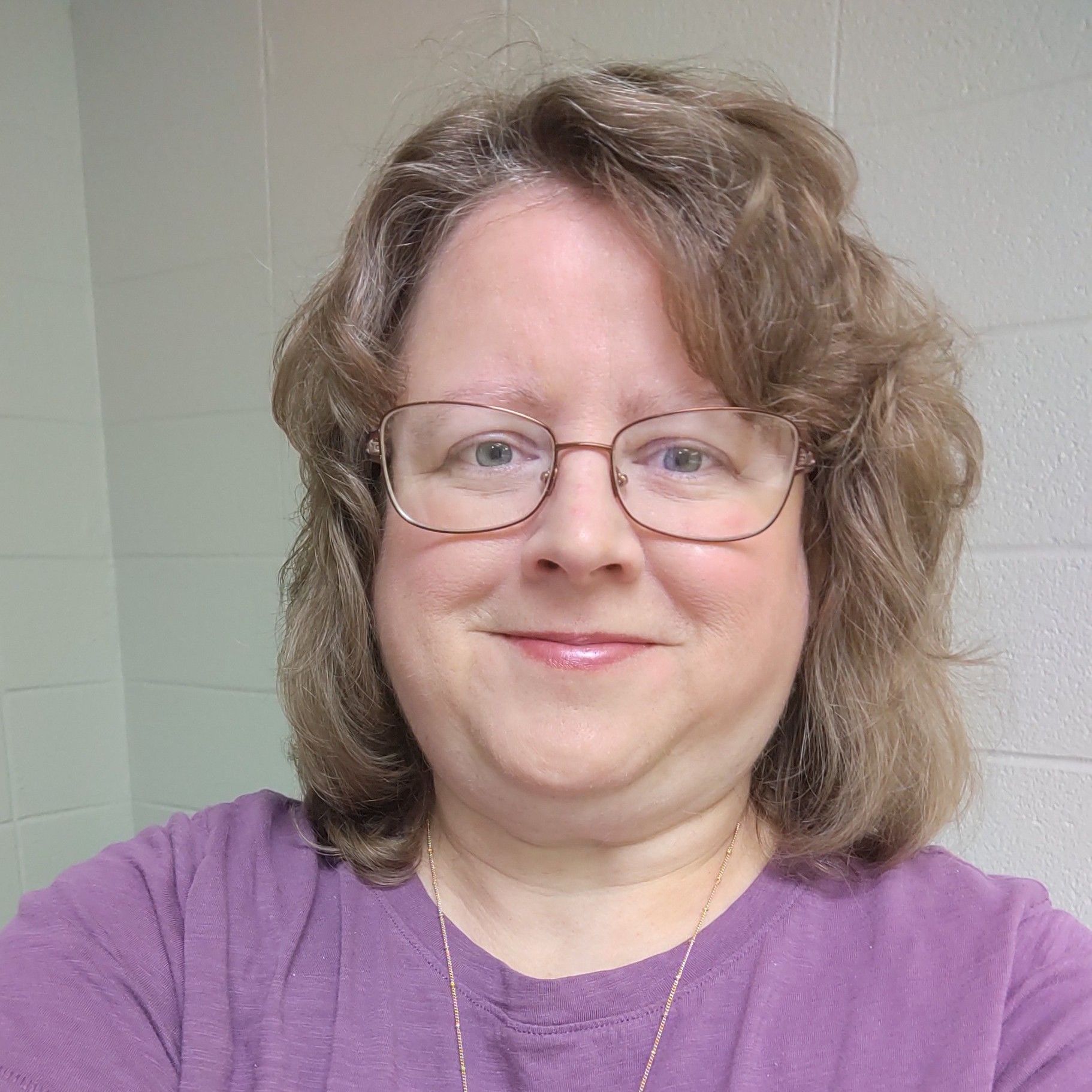 a woman wearing glasses and a purple shirt is smiling for the camera .