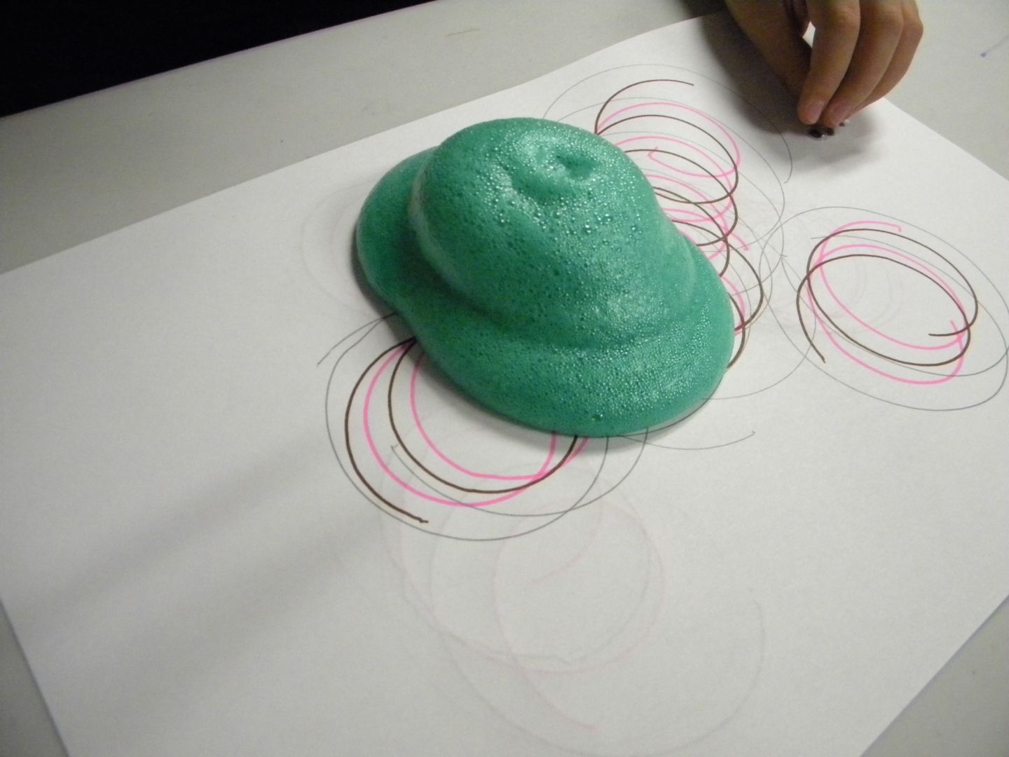 A person is drawing circles on a piece of paper with green slime