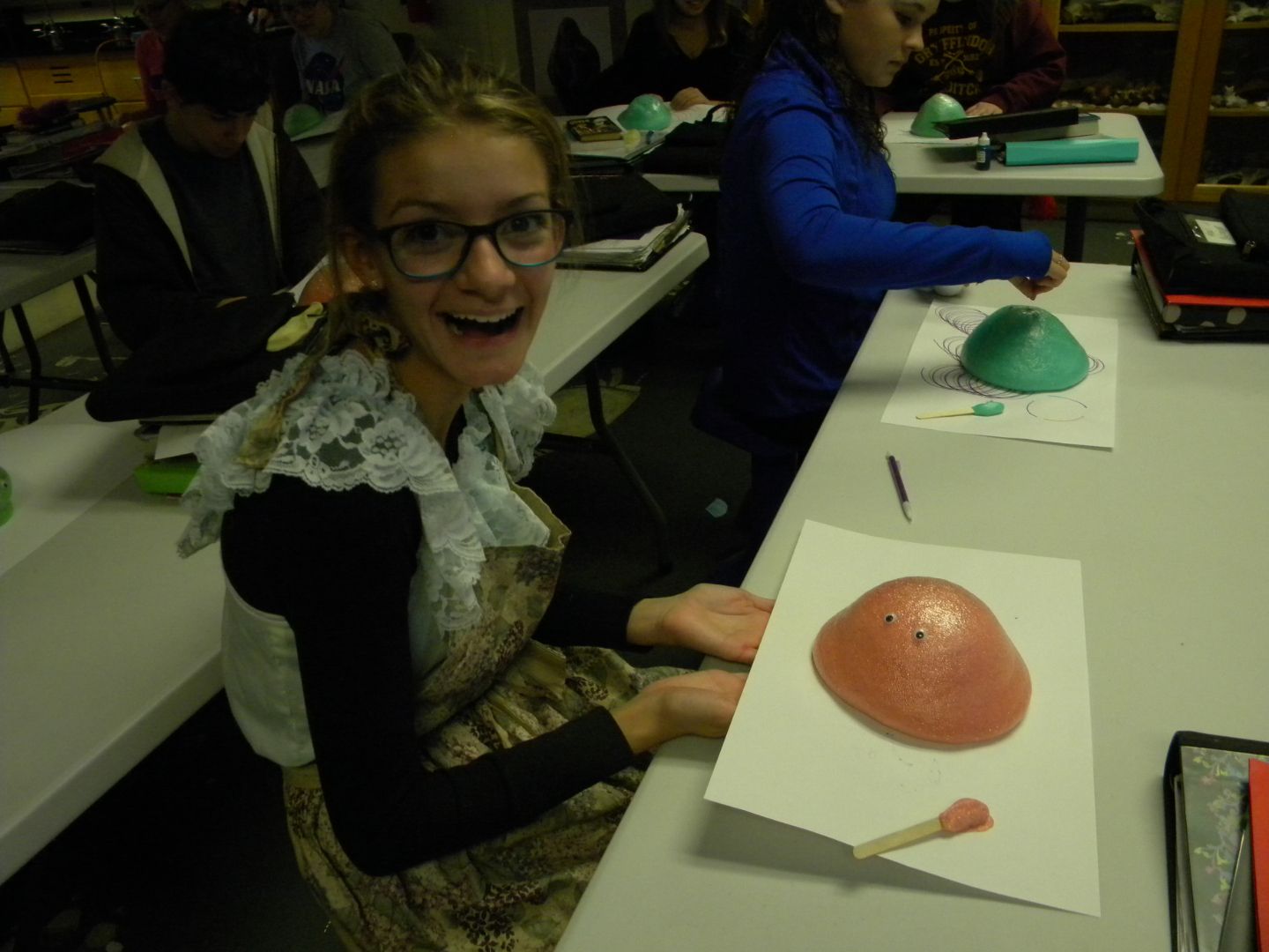 A girl with glasses sits at a table holding a piece of paper