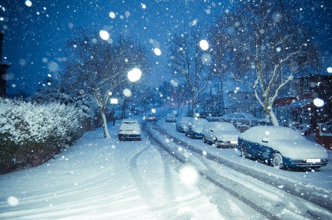 A snowy street with cars covered in snow