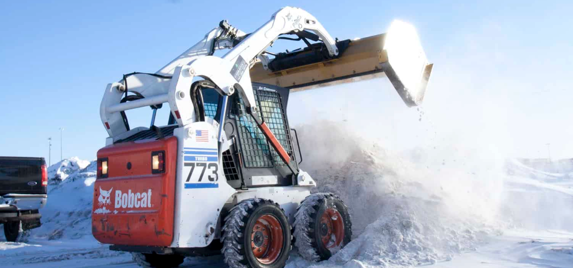 A bobcat skid steer is clearing snow from a snowy field.