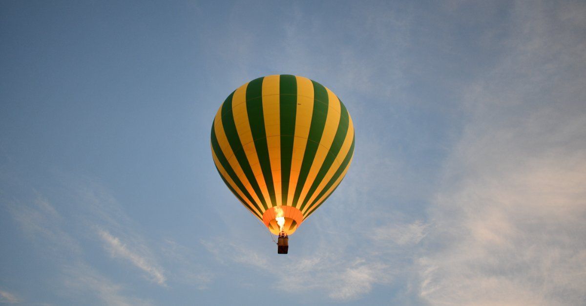 A green and yellow striped hot air balloon floating against a blue sky, illuminated by its burner at