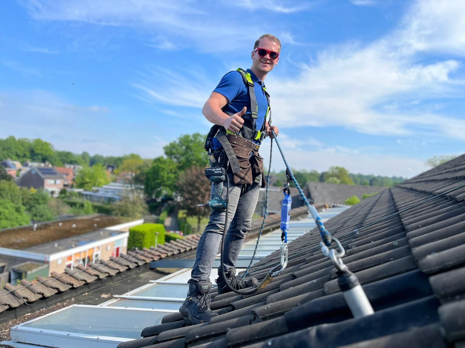 Worker in safety gear on a sloped roof, inspecting shingles under a blue sky.
