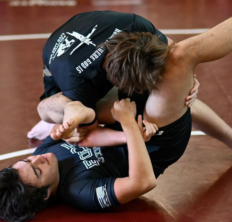 Two wrestlers grappling on a red mat. One is on top, holding the other in a body lock.