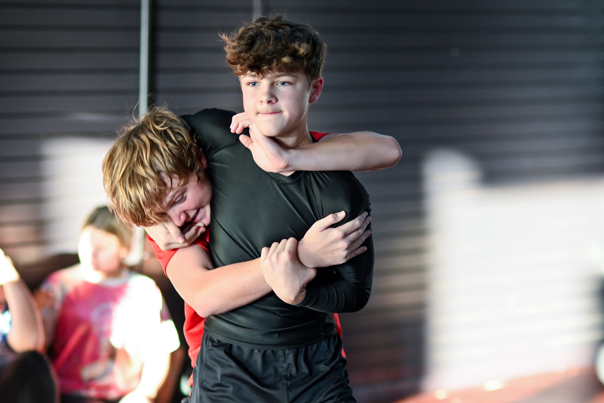 Two young athletes grappling in a training setting. One has the other in a headlock.