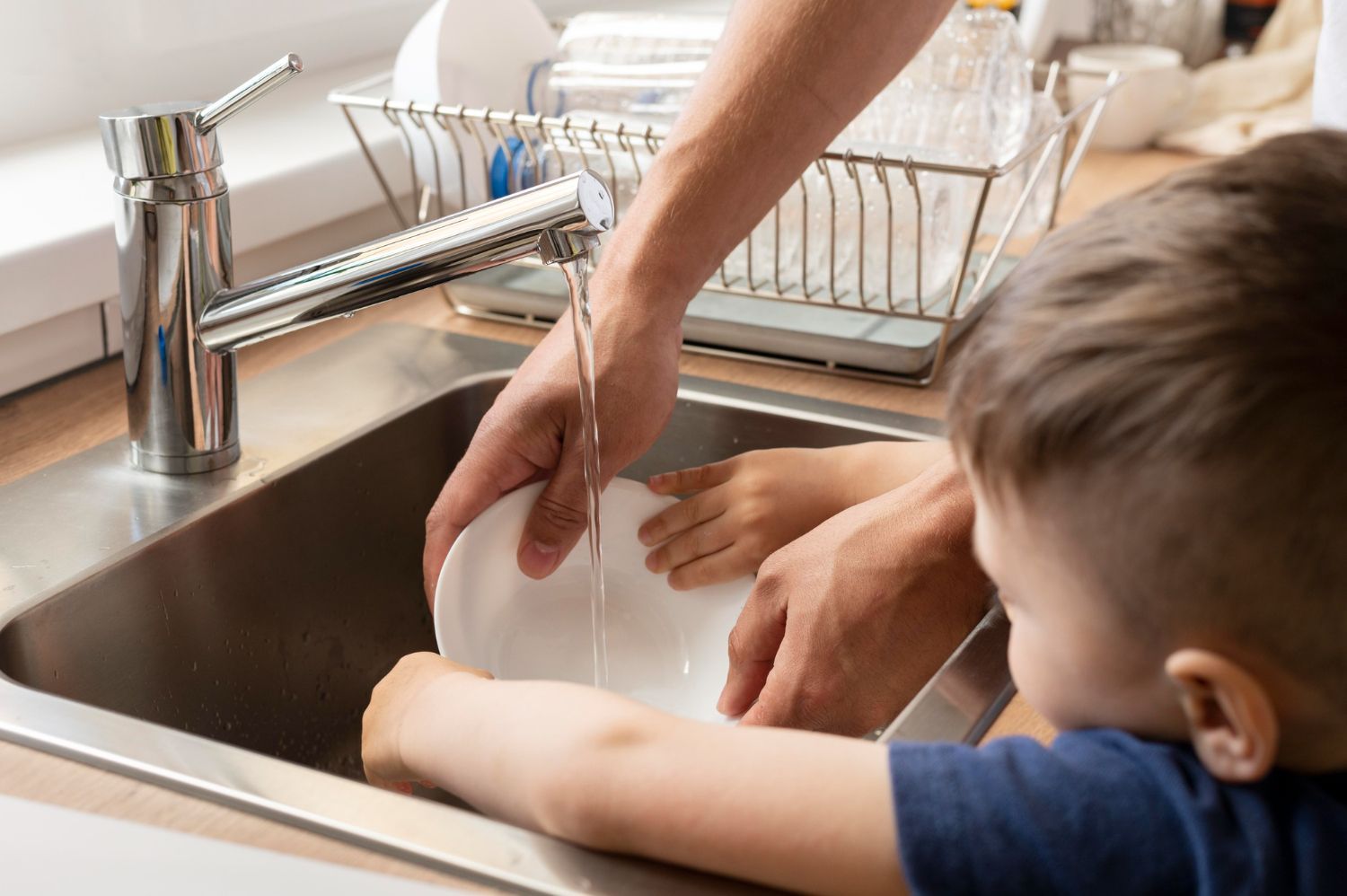 A man and a boy are washing dishes in a kitchen sink.