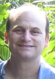 A man with a bald head and a blue shirt is smiling for the camera.