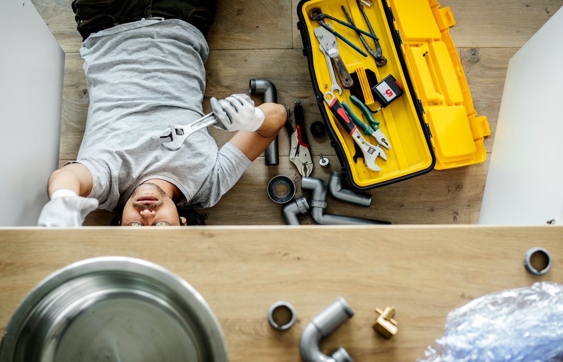 A man is laying on the floor fixing a sink.