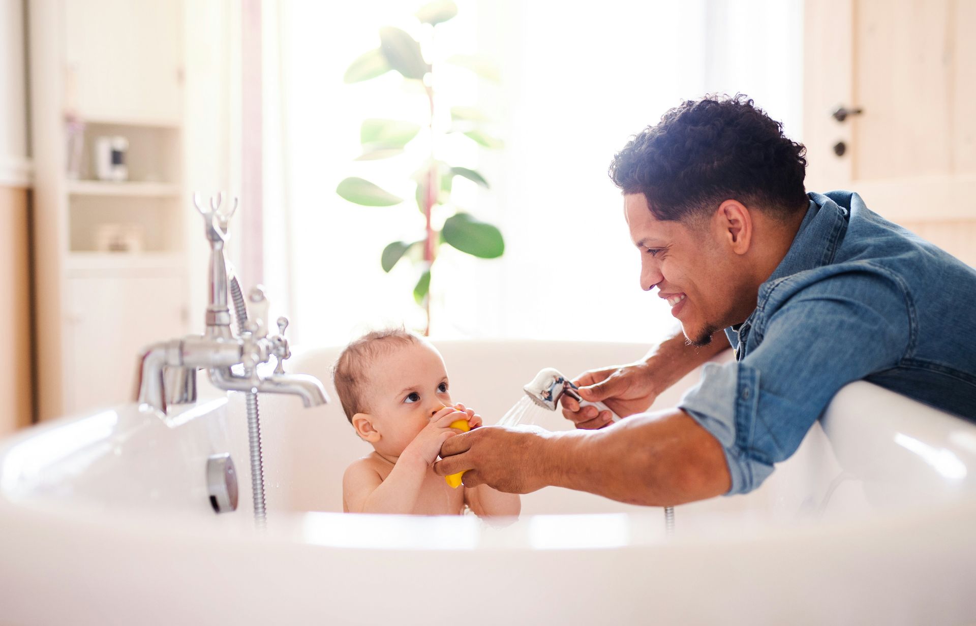 A man is taking a bath with a baby in a bathtub.