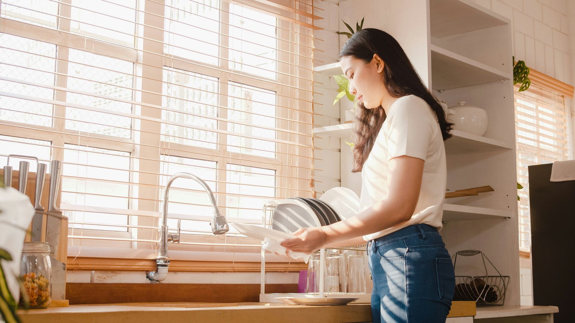 A woman is washing dishes in a kitchen sink.