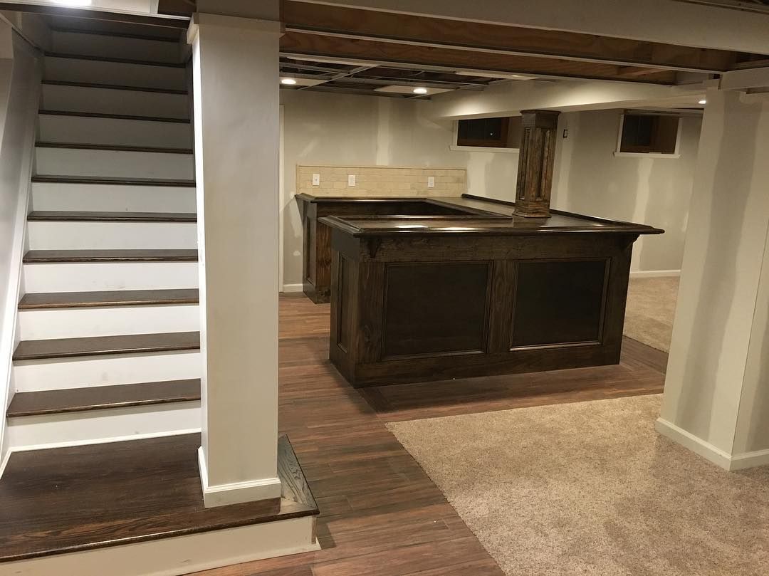 Basement with wooden bars, stairs, and exposed beams. Beige carpet and wood flooring.