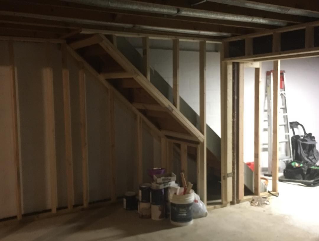 Unfinished basement with wooden stair framing, bare studs, and doorway to another room.