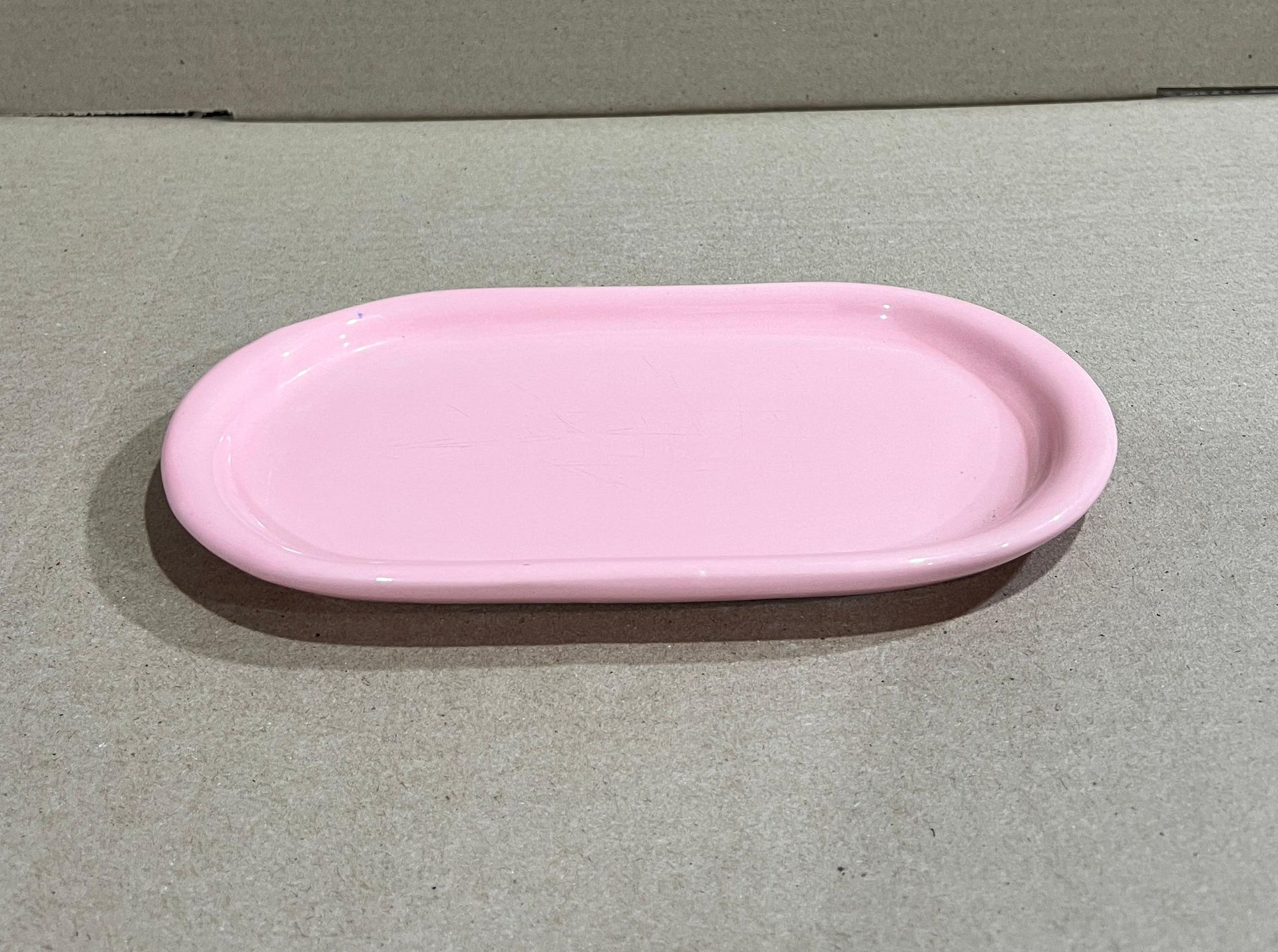 Bandeja de cerámica de color rosa, de forma ovalada, sobre una superficie gris claro.