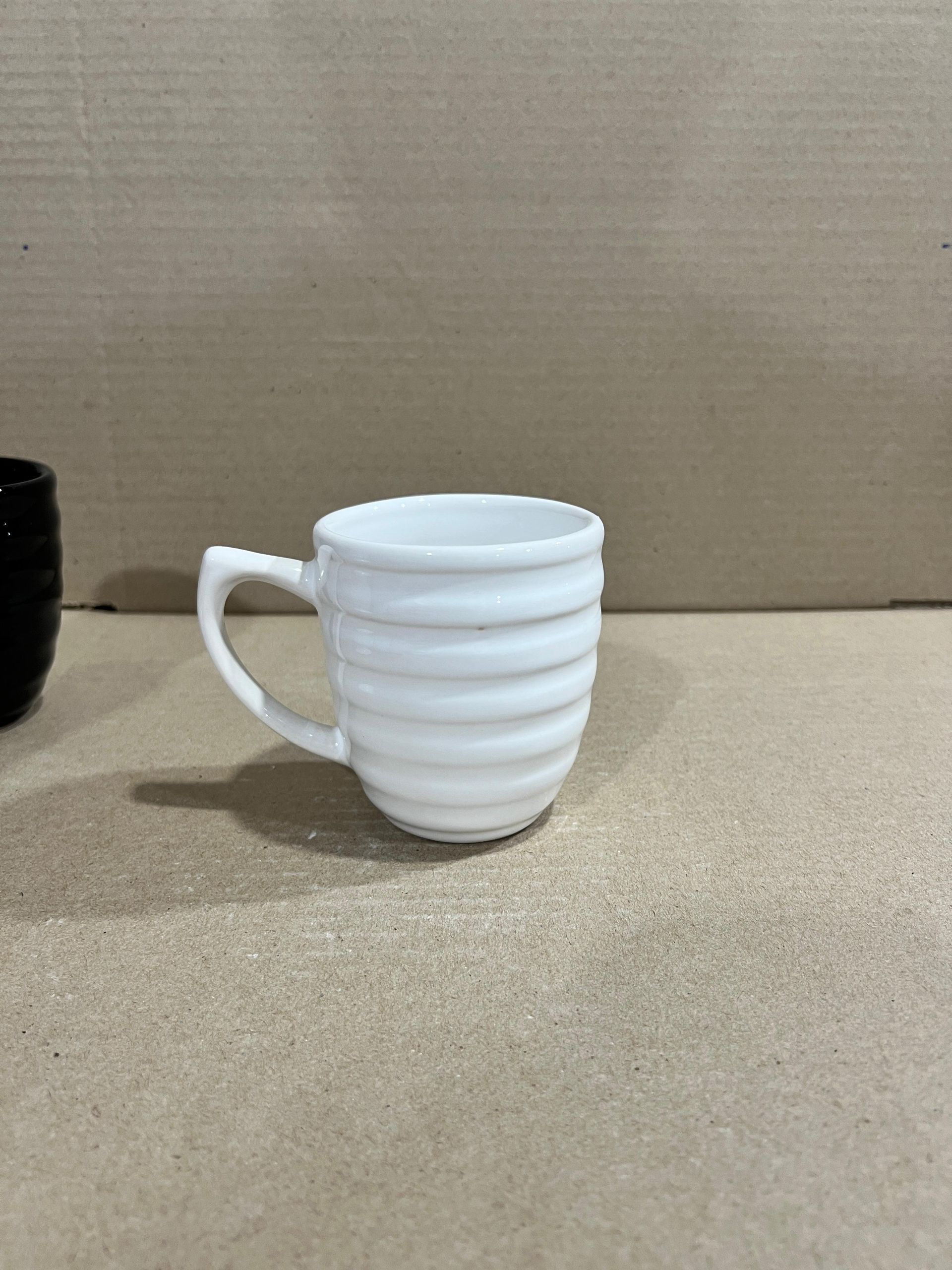 Taza de cerámica blanca con cuerpo estriado sobre superficie de color marrón claro.