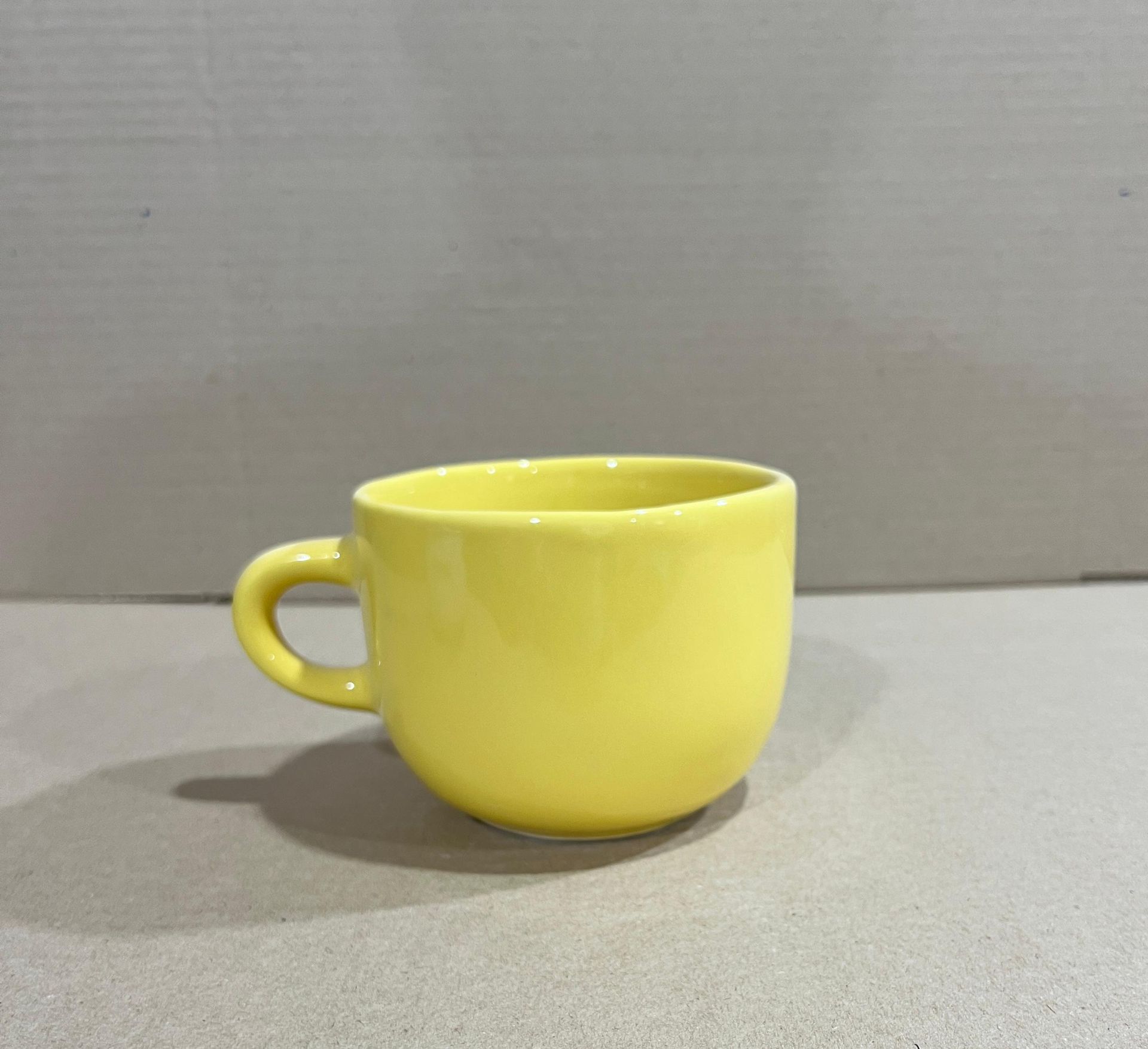 Taza de té amarilla sobre una superficie neutra.