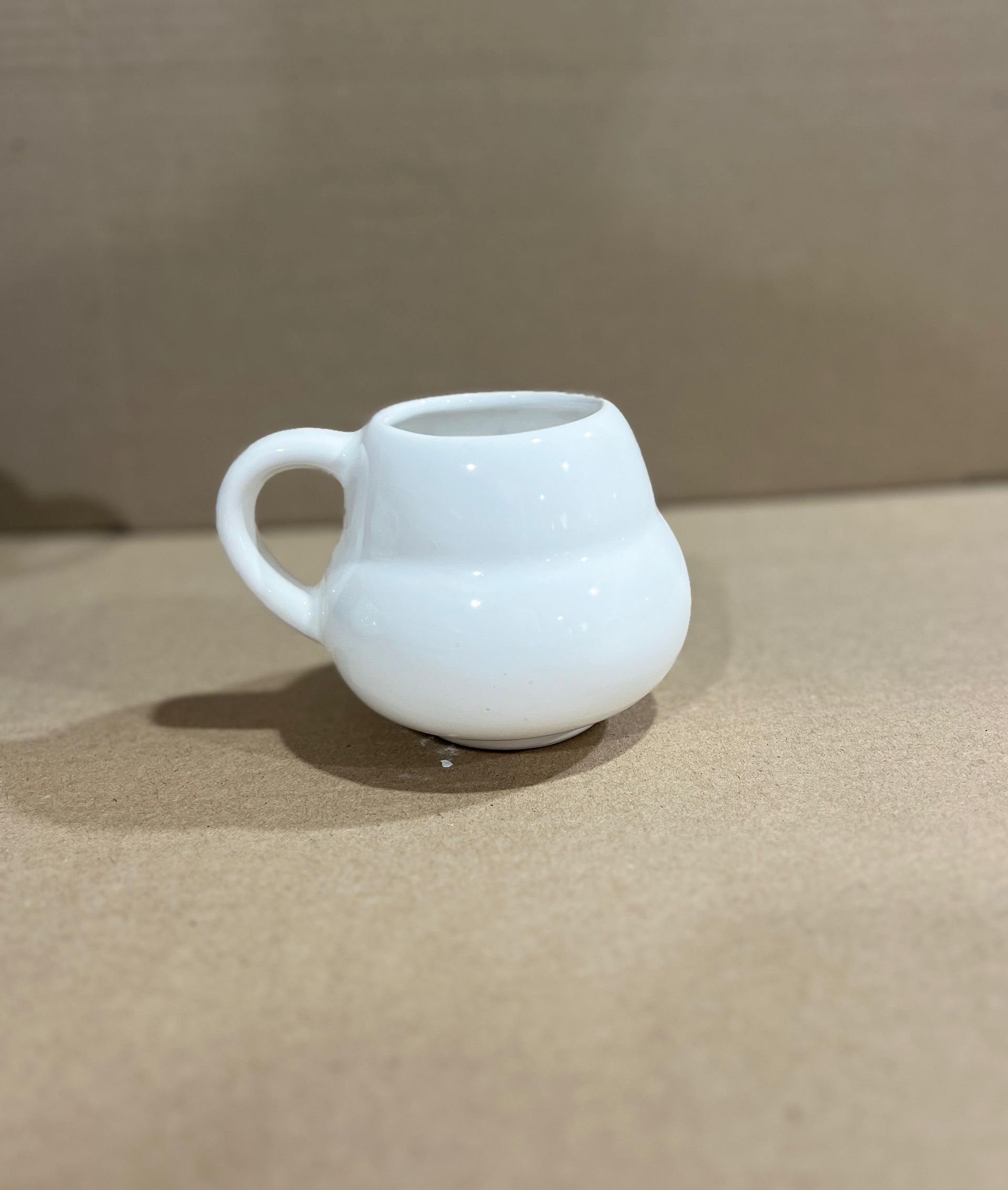 Taza miniatura de cerámica blanca con base redondeada y asa pequeña.