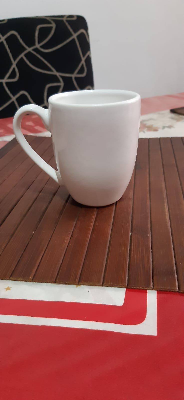 Taza blanca sobre un mantel de madera, sobre una superficie roja y blanca.