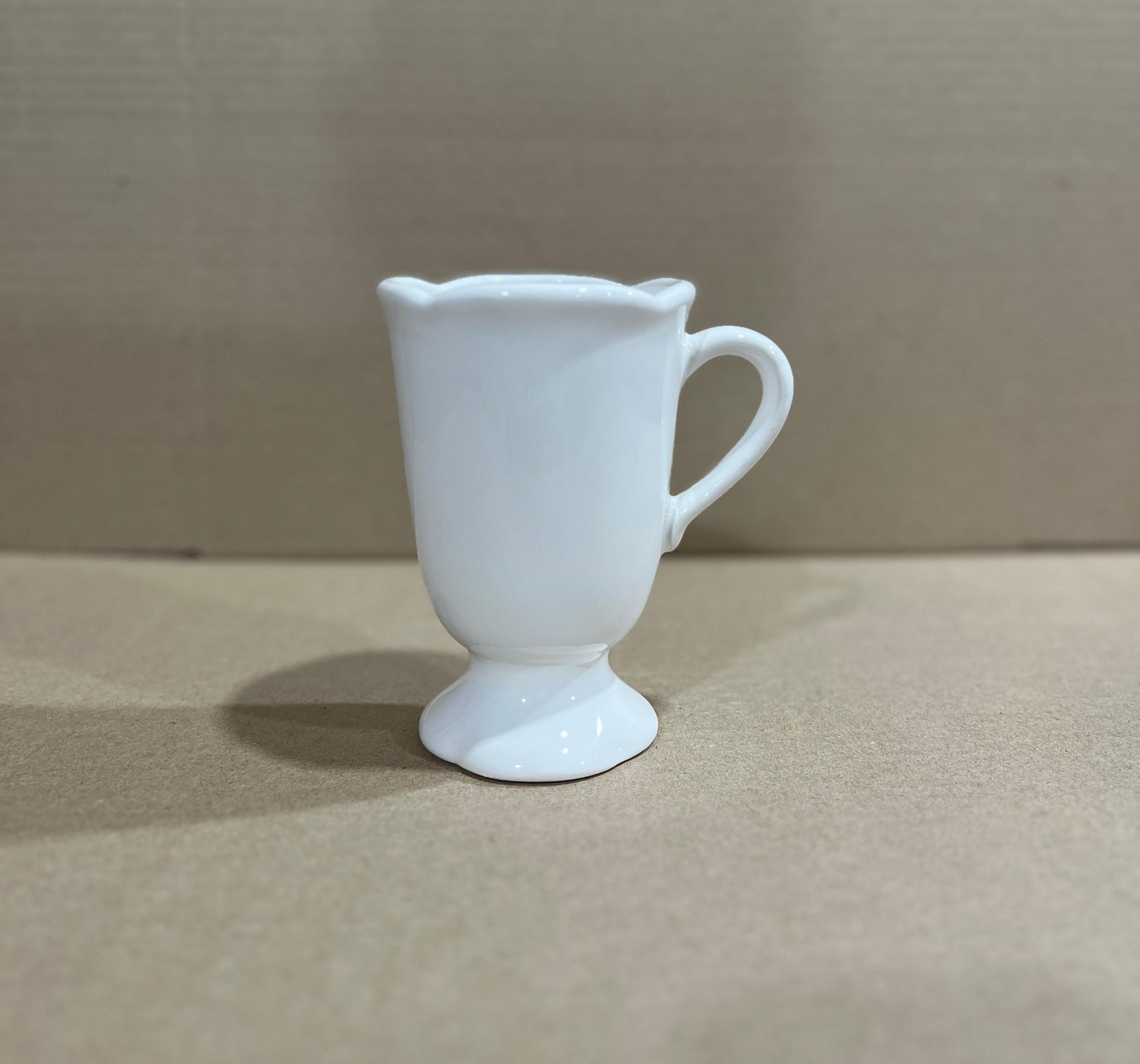 Taza con pedestal blanco y borde festoneado.