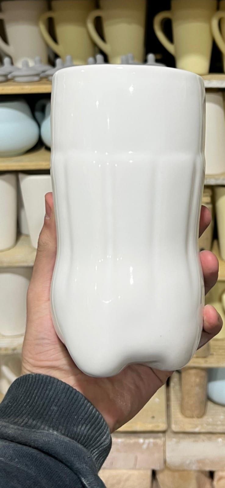 Una persona sostiene una taza de cerámica blanca con una forma única en un taller de cerámica
