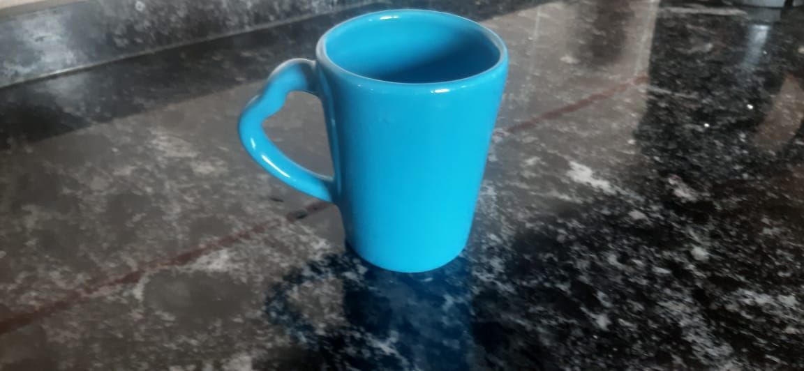 Taza azul con asa en forma de corazón sobre una encimera negra.