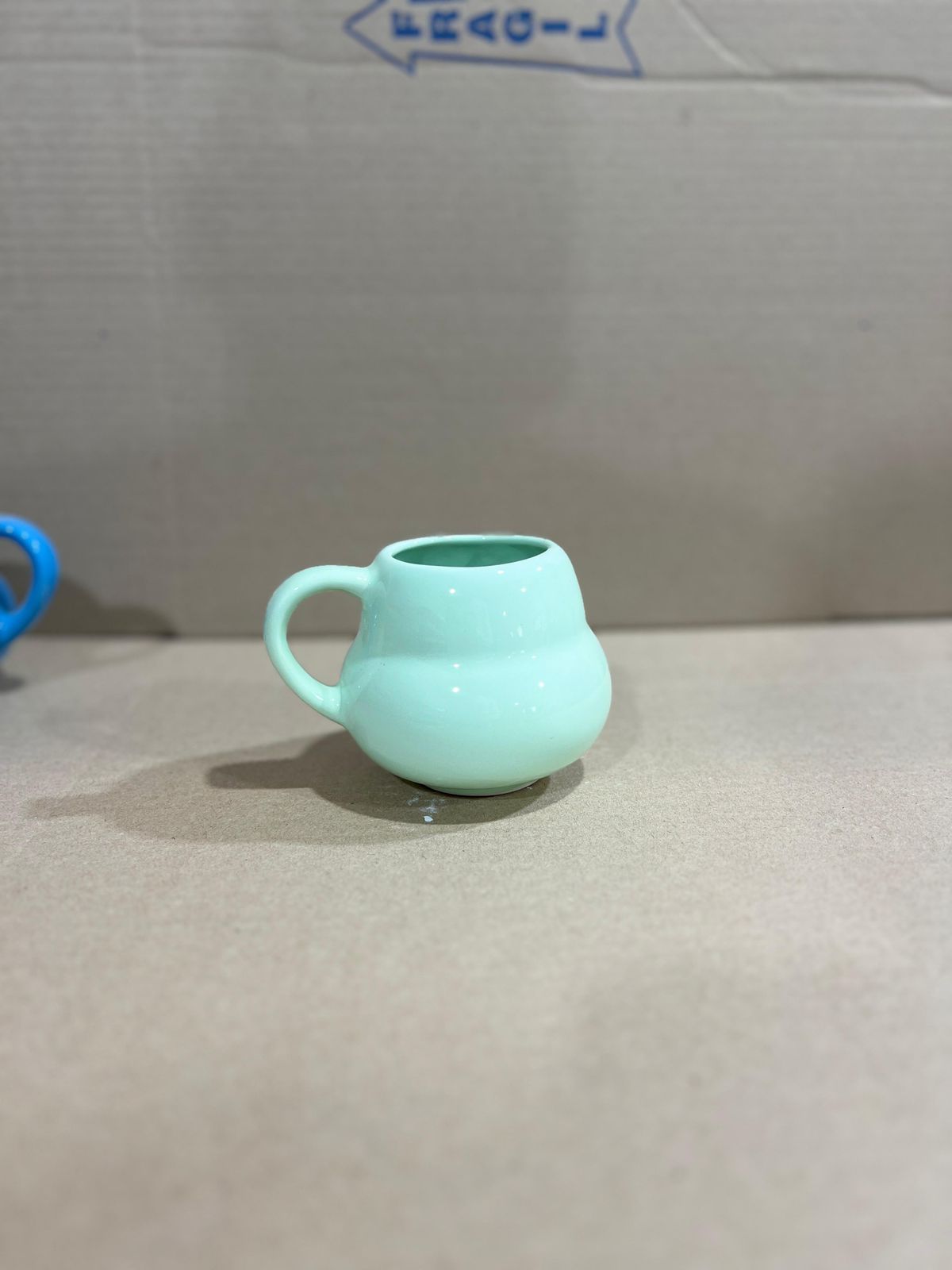 Taza de cerámica de color amarillo con cuerpo y asa redondos, sobre superficie gris claro.