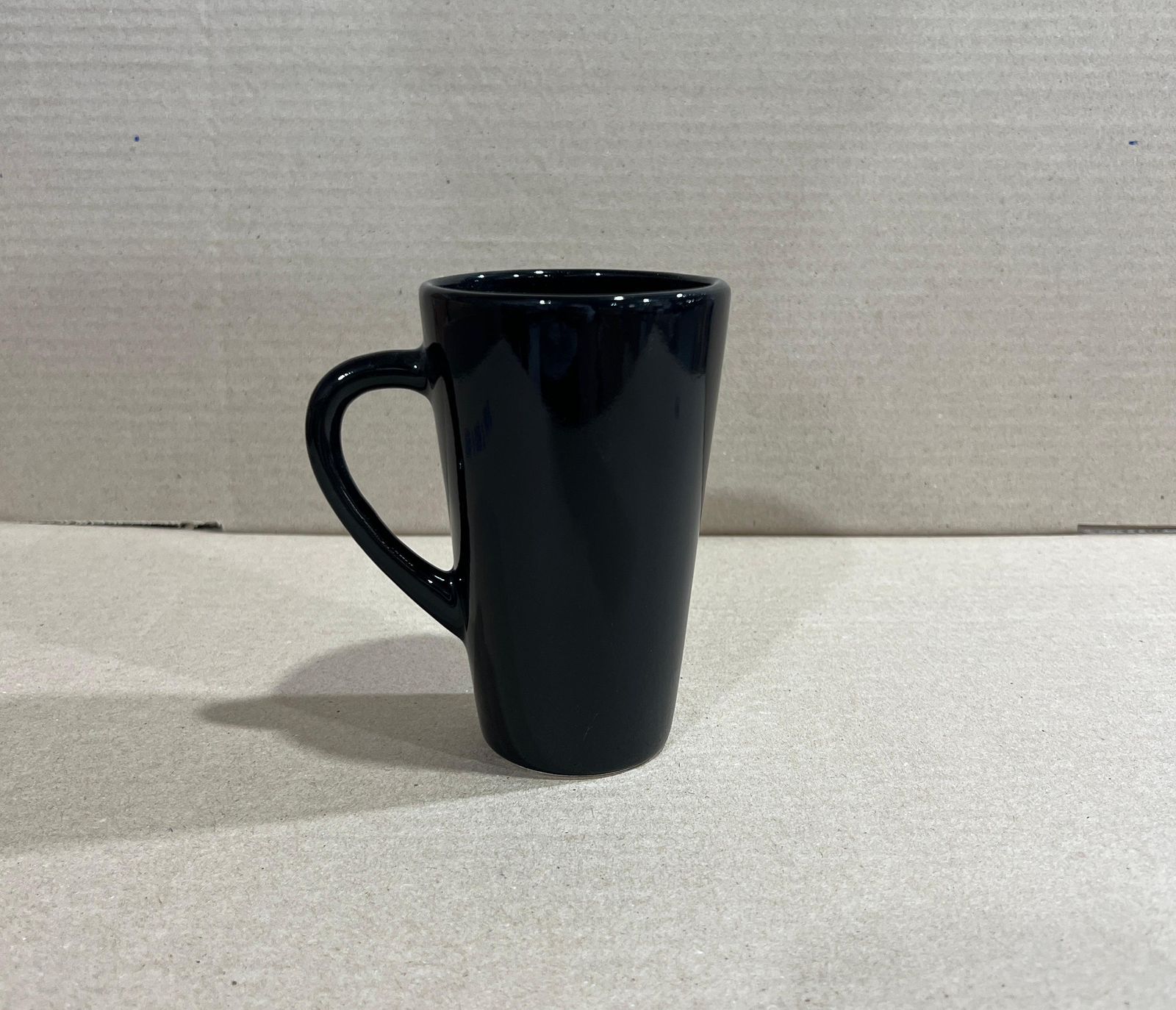 Taza de cerámica de color verde menta con asa curvada, colocada sobre una superficie de color claro.