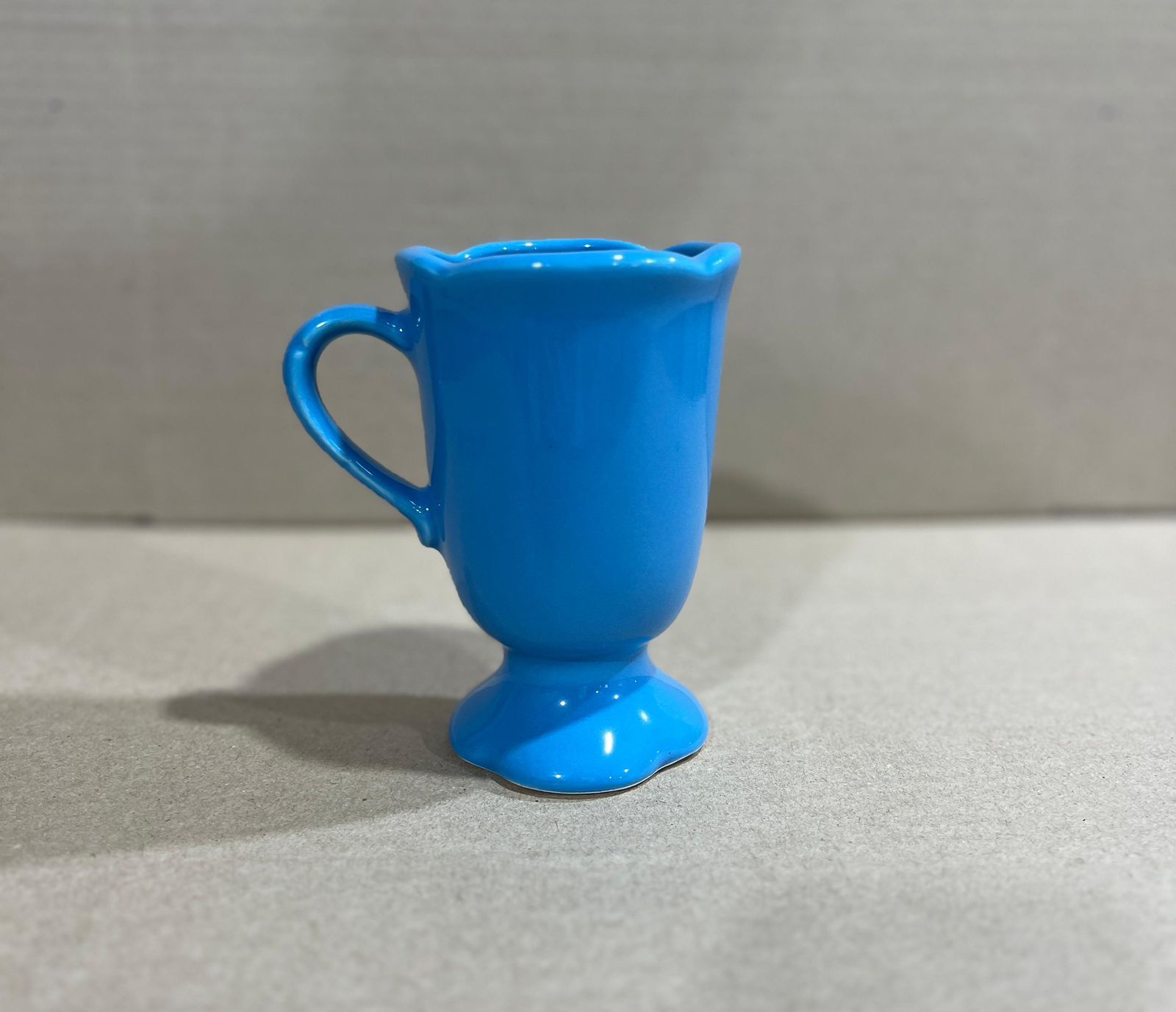 Taza de cerámica rosa con borde festoneado y base de pedestal sobre una superficie neutra.