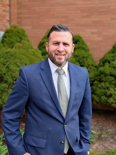 Pastor Joel Beharry standing outdoors in front of shrubbery.