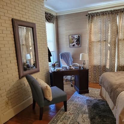 Bedroom with desk, chair, mirror, and bed. Brick-patterned wall and patterned rug.