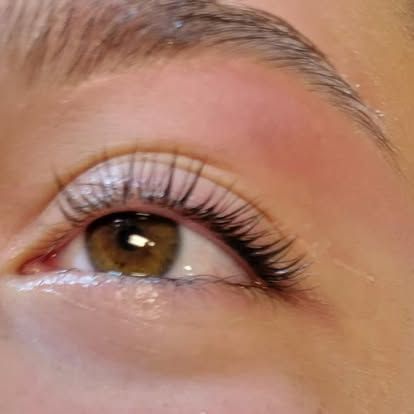 Close-up of an eye with lifted lashes, brown iris, and a light eyebrow.