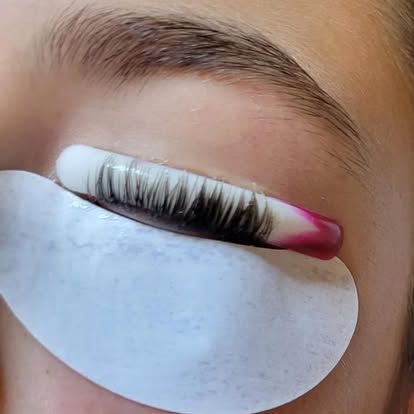 Close-up of an eye with eyelashes glued to a pink and white curler during a lash lift procedure.