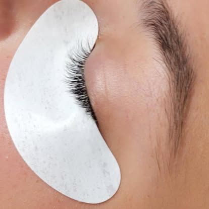 Eyelash extensions in progress: eye with a white under-eye pad, black lashes, and a brown eyebrow.